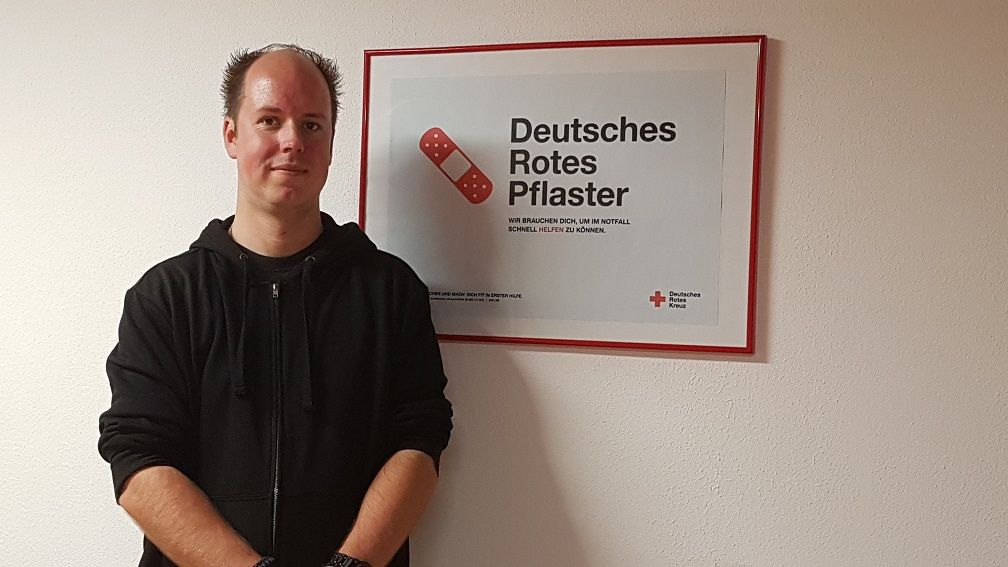 Bild: Der neue Bereitschaftsleiter Sascha Finkel steht vor einer weißen Wand mit DRK-Bild